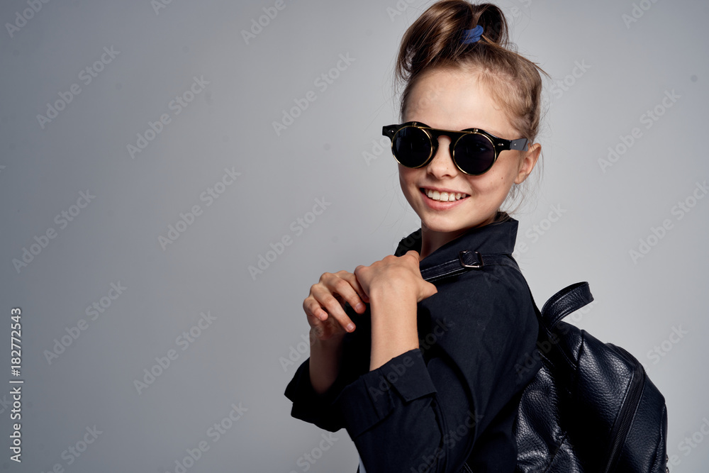 a little girl in black glasses and a jacket on a gray background. empty space for copying a little girl in black glasses and a jacket on a gray background. empty space for copying