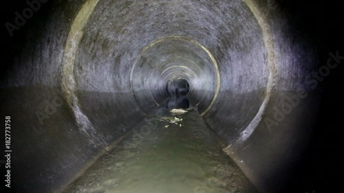 Dark underground sewer round concrete tunnel. Industrial wastewater and urban sewage flowing throw sewer pipe