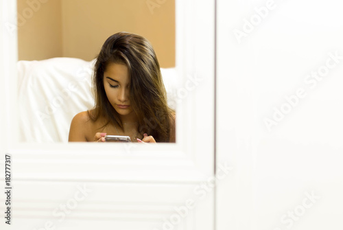 Reflective on mirror mixed race woman sitting on the floor and using smartphone