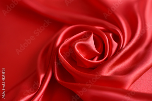 Close up of ripplesin shape of rose flower in red silk fabric. Satin textile background.