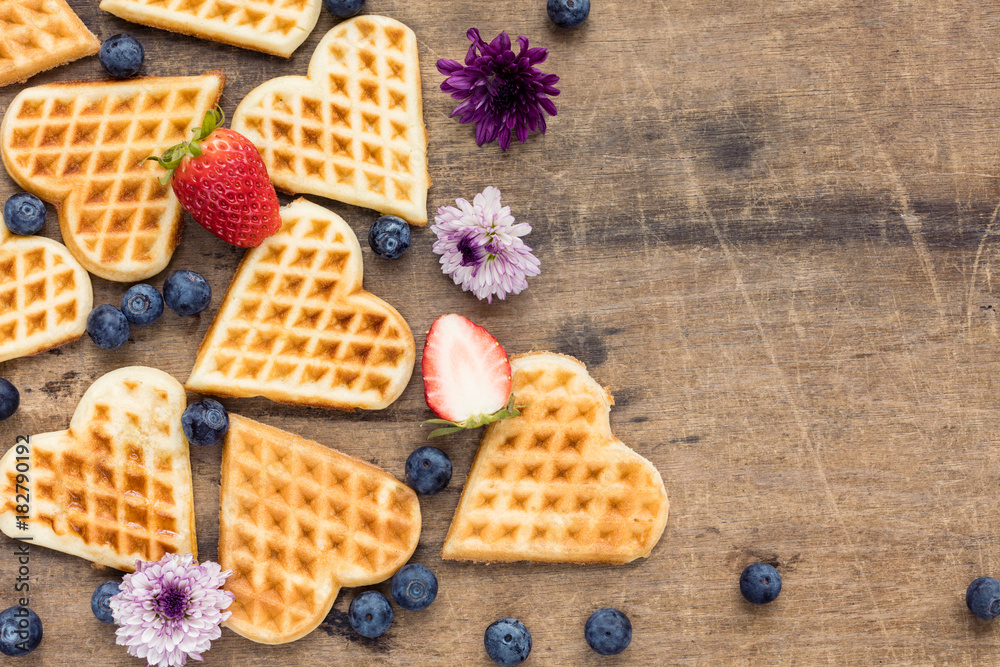 Homemade heart shape waffles with blueberries and strawberry on wooden background, top view Homemade heart shape waffles with blueberries and strawberry on wooden background, top view