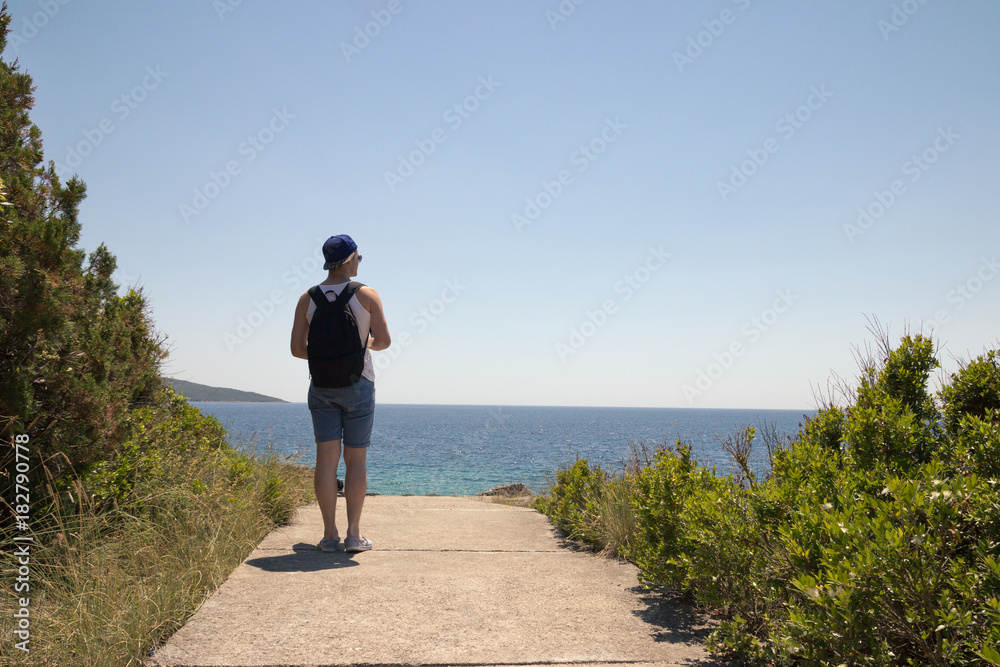 one young man back, rear view, outdoor standing near lake sea, looking at coast.