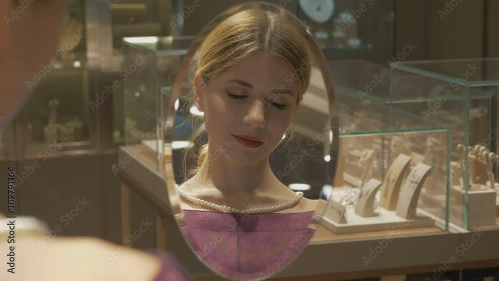 A young beautiful girl is considering a pearl necklace in a jewelry store. A young beautiful girl is considering a pearl necklace in a jewelry store.