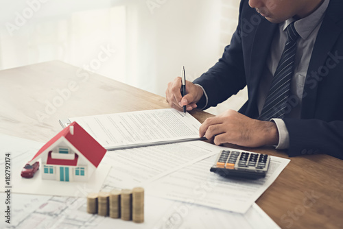 Businessman signing contract agreement with money and house model on the table photo