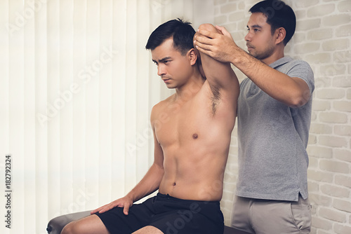 Therapist training rehab exercise, overhead tricep stretching, to athlete male patient in hospital