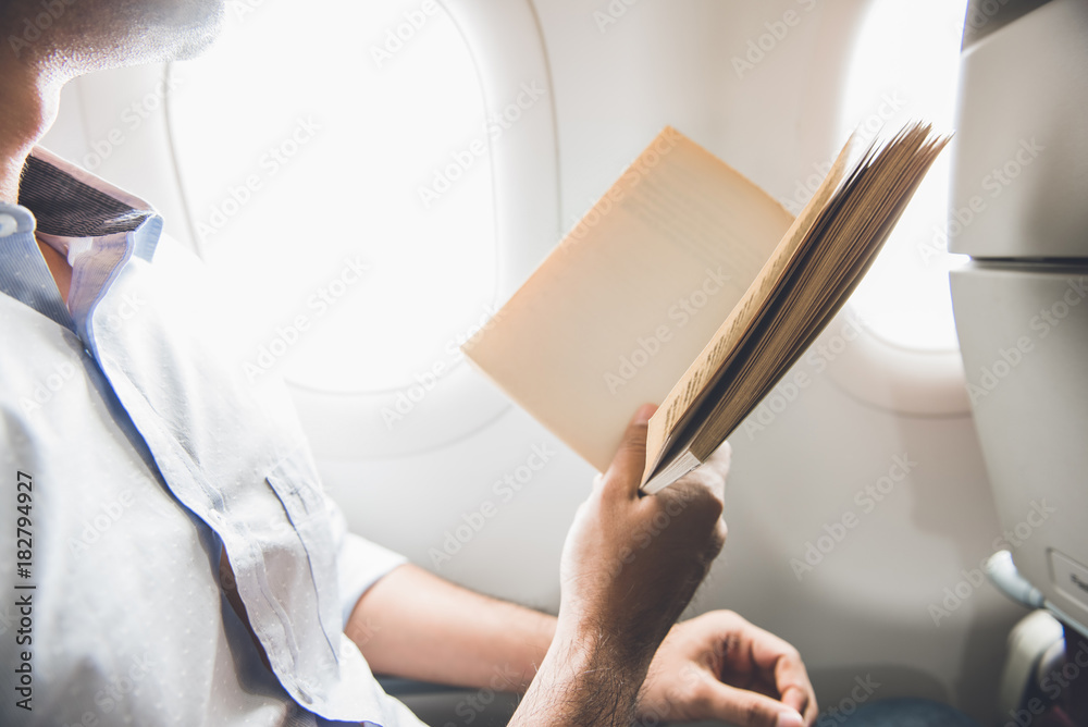 Male passenger killing time by reading book while traveling on the airplane Male passenger killing time by reading book while traveling on the airplane