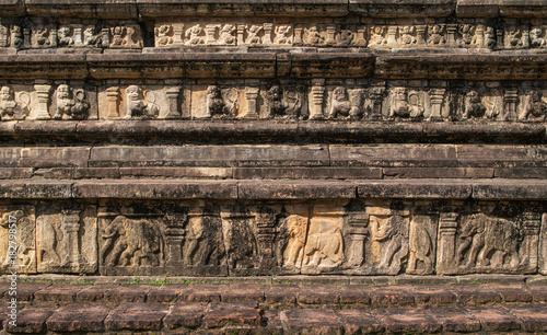 Fragment of a wall of an ancient palace or temple with the bas-relief representing rows of elephants, lions and mythical people. A mystical background for storytelling in a genre of 'lost'. 