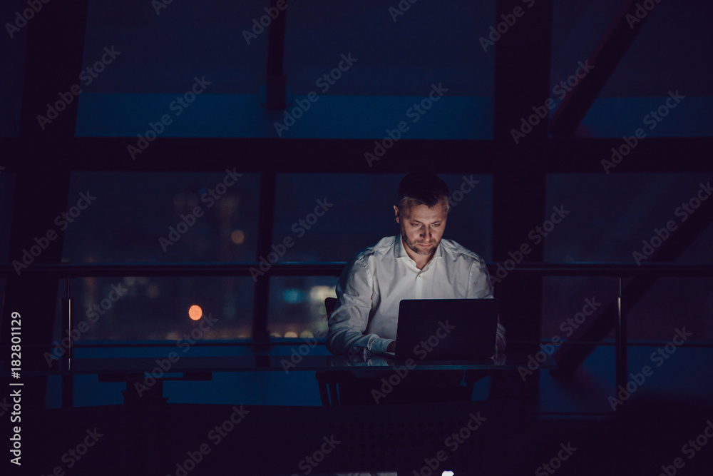 Businessman working on laptop in night office. - obrazy, fototapety, plakaty 