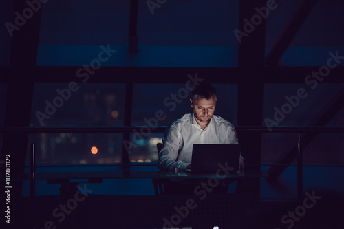 Businessman working on laptop in night office.