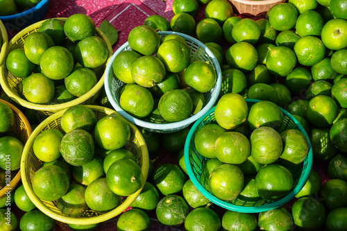 Fototapeta Naklejka Na Ścianę i Meble -  Baskets of fresh rounded organic lime fruit background in bright yellow and green color selling in market under sunlight with light reflection skin and shadow