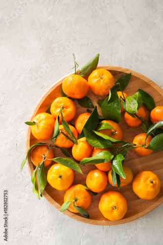 Plate of fresh and juicy tangerines with leaves on a white stone background. Top view and copy space. © galiyahassan