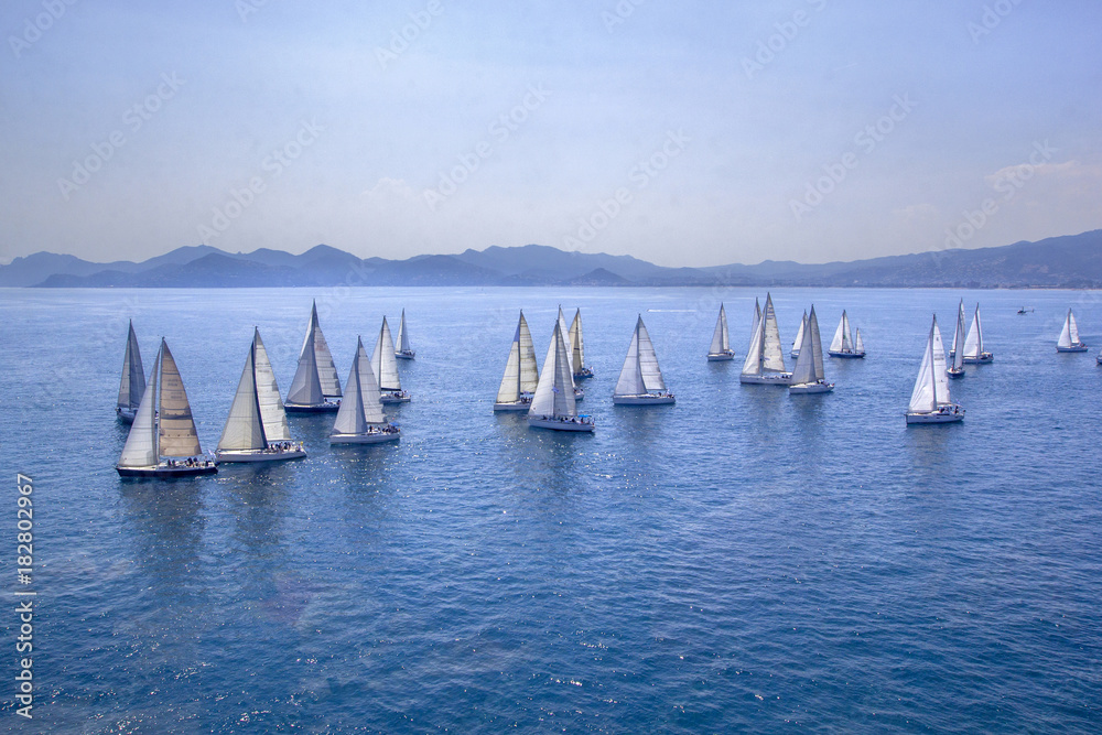 Obraz premium Sailing regatta or a group of small water racing boats in the Mediterranean, a panoramic view with blue mountains on a horizon