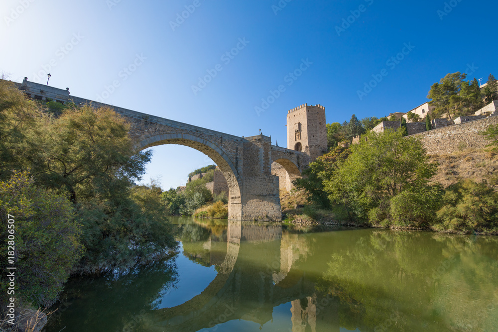 Green water river Tagus, Tajo in Spanish, Alcantara arch bridge and door,  landmark and monument from ancient Roman age, in Toledo city, Spain, Europe
