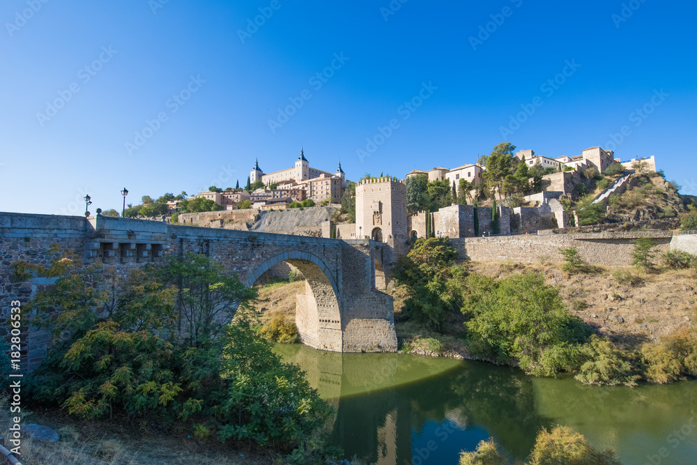 Green water river Tagus, Tajo in Spanish, Alcantara arch bridge and door,  landmark and monument from ancient Roman age, and alcazar, in Toledo city, Spain, Europe
