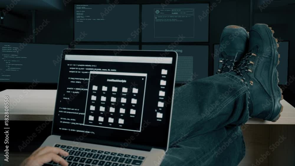 Hacker feet up to table. Hacker with laptop coding exploit to crack code. Tracing contact and satellite upling through internet. Man in military shoes sits and feet up on desk. Laptop computer screen.