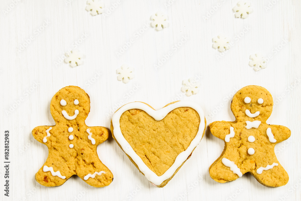 Gingerbread men friends near the heart on a white wooden table. Gingerbread men friends near the heart on a white wooden table.