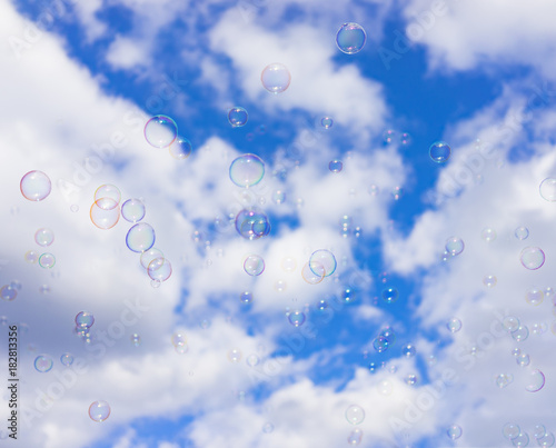 Abstract background : Beautiful soap bubbles reflecting various color floating on blue sky and white cloud background.