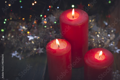 A romantic festive still life with red burning candles of different size. White and red colors. Blurred pine tree on the back. Blurred bokeh
