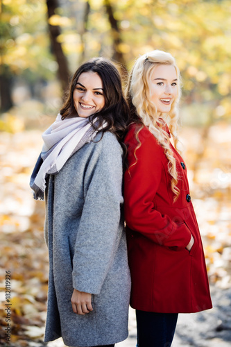 Full length portrait of a young woman posing with girlfriend in autumn park