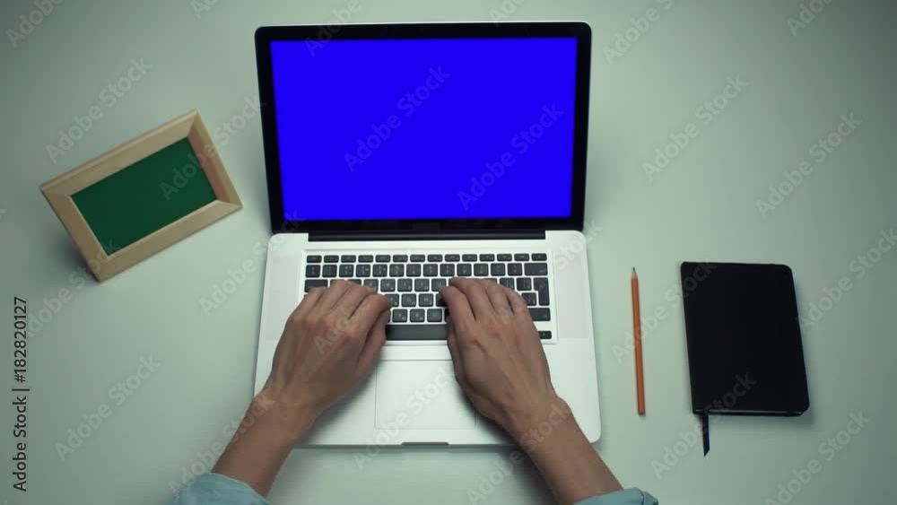 Man using laptop computer with green screen at white desk Man using laptop computer with green screen at white desk