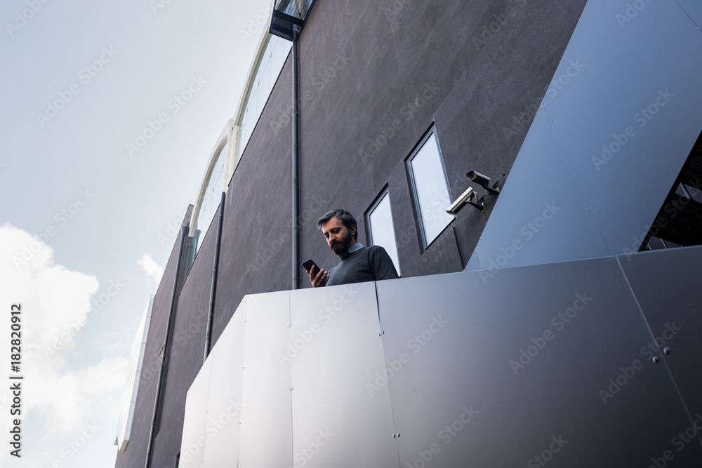 Φωτογραφία Young adult business man looking at smartphone standing on black metal outside s