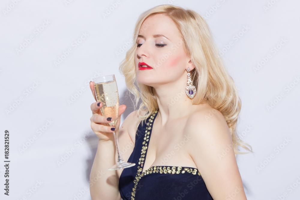 Studio portrait of a beautiful young blonde woman in a blue long evening dress. A girl is holding a glass of champagne in her hands Studio portrait of a beautiful young blonde woman in a blue long evening dress. A girl is holding a glass of champagne in her hands