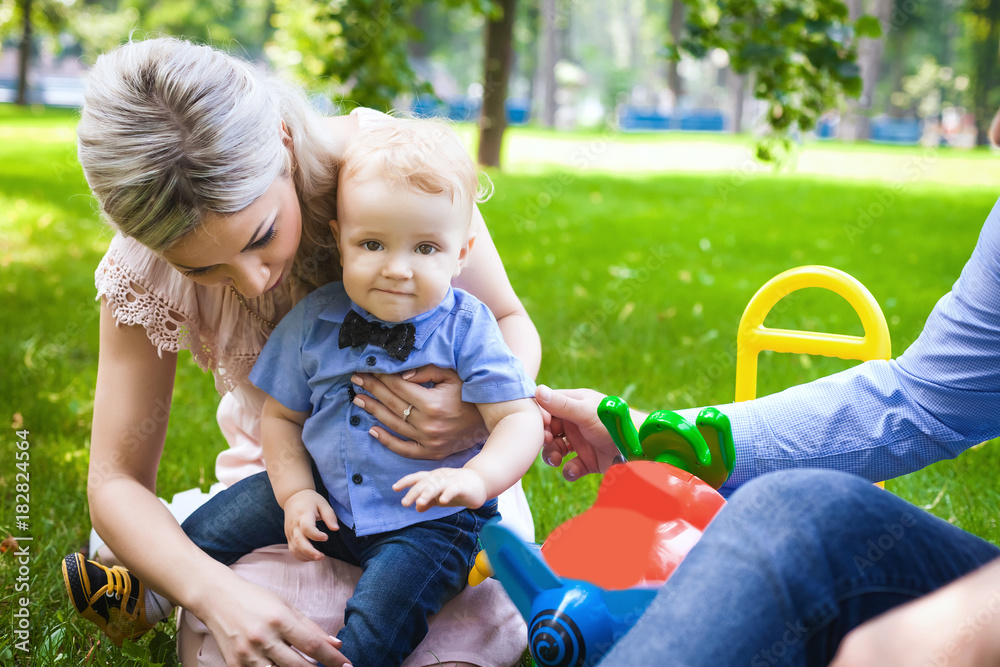 joyful family sitting on grass in city park, lovely couple with their little son have rest in attraction park, concept of happy family joyful family sitting on grass in city park, lovely couple with their little son have rest in attraction park, concept of happy family