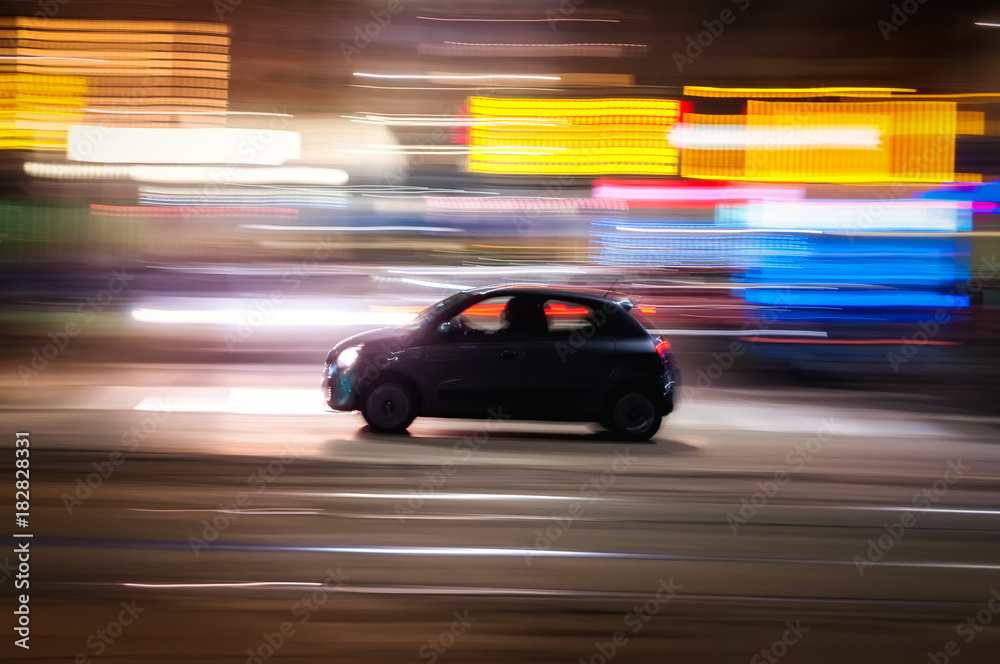 Automobile che sfreccia veloce di notte per le vie con luci colorate di una  grande città 