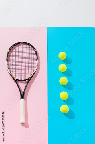 top view of tennis racket on pink and yellow balls in row on blue © LIGHTFIELD STUDIOS
