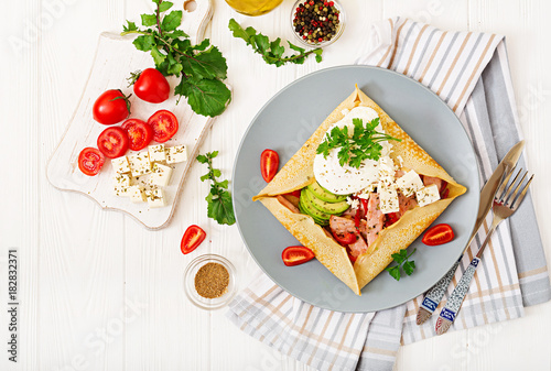 French cuisine. Breakfast, lunch, snacks. Pancakes with egg poached, feta cheese, fried ham, avocado and tomatoes on white table. Top view