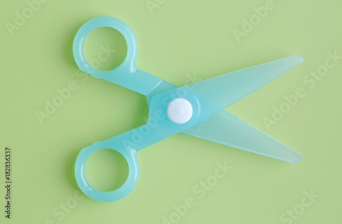 Cyan Plastic children safety scissors on green background.