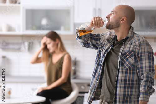 Man drinking alcohol and blurred woman at home