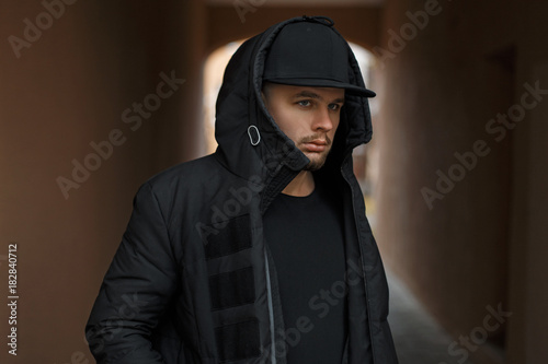Photography Stylish young man in a baseball cap in a black winter warm jacket with a hood on