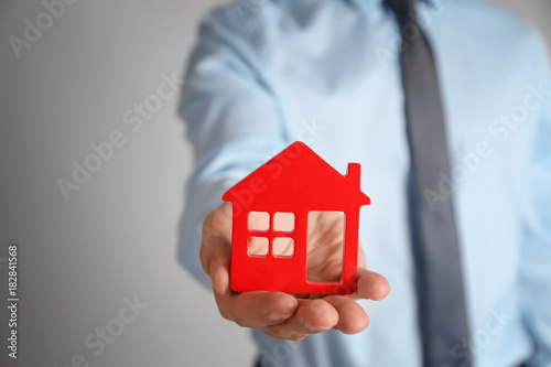 Real estate agent holding house model on color background