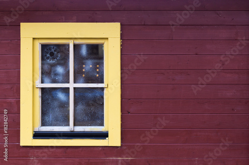 Christmas fair cabin's window with snow pattern on brown wooden wall with copy space. Light yellow window with brown plank background © Woody Alec