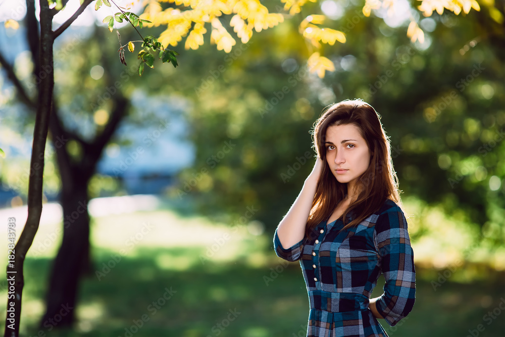 A woman in long checkered dress. Romantic girl in the spring park. A woman walks in the park in a casual dress. Green field on vackground. Vertical orientation. Copy space A woman in long checkered dress. Romantic girl in the spring park. A woman walks in the park in a casual dress. Green field on vackground. Vertical orientation. Copy space