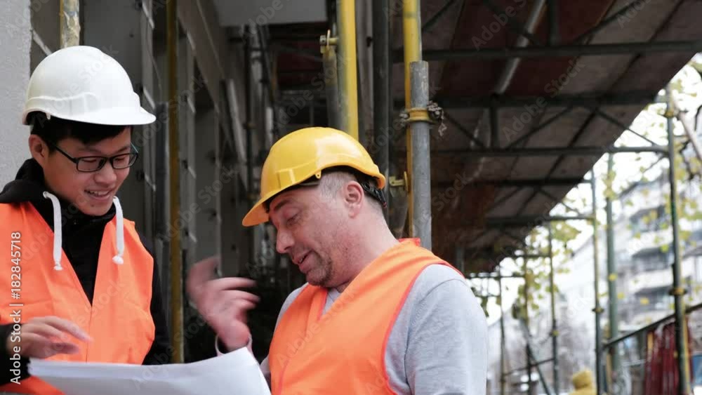 Young Asian apprentice engineer at work on construction site with the senior manager. Outdoors Young Asian apprentice engineer at work on construction site with the senior manager. Outdoors