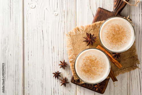 Homemade eggnog with grated nutmeg and cinnamon on white wooden table. Traditional Christmas drink.