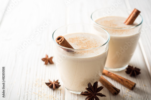 Homemade eggnog with grated nutmeg and cinnamon on white wooden table. Traditional Christmas drink.