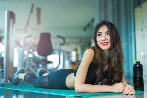 Sports woman lying and relaxing on yoga mat in fitness gym with sports equipment background. Beauty and Workout training exercise concept. Body build up and Strength theme.