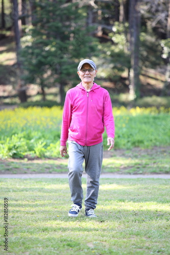 senior Japanese man in pink wear walks on a lawn 