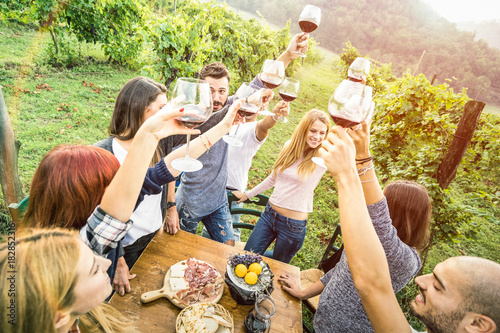 Young friends having fun outdoors drinking red wine glasses - Happy people eating seasonal local food at harvest time in farmhouse vineyard winery - Youth friendship concept on warm vintage filter photo