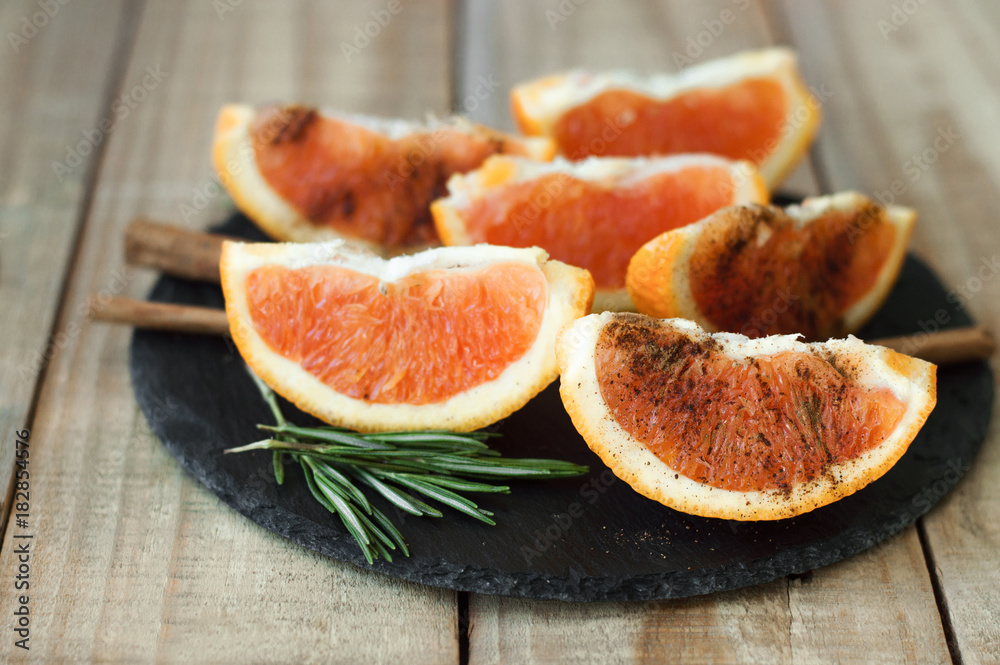 Orange with cinnamon powder and rosemary served on black slate board on wooden table. Portion of sliced orange fruit. Healthy dessert Orange with cinnamon powder and rosemary served on black slate board on wooden table. Portion of sliced orange fruit. Healthy dessert