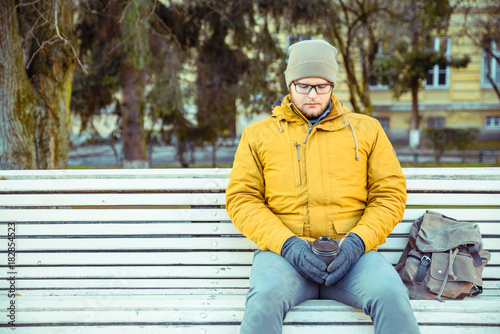 man waiting on the bench of city park with cup of coffe