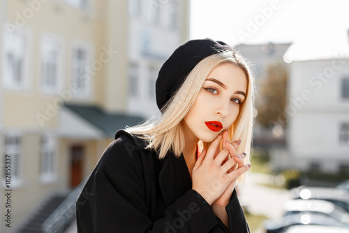 Fashionable portrait of a beautiful blonde woman in a black coat and a black beret on a sunny day photo