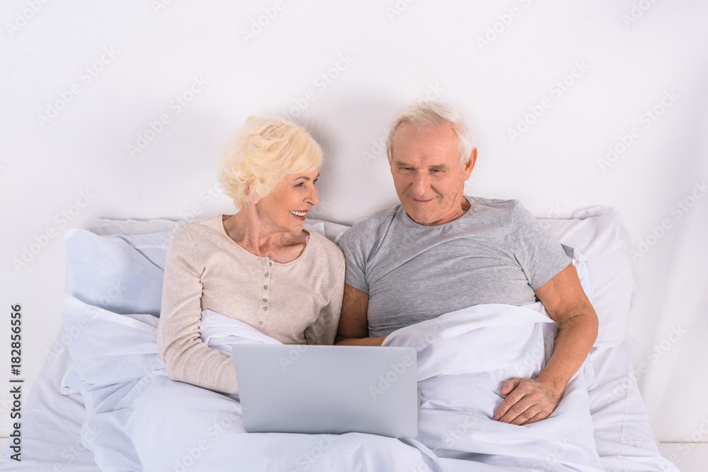 senior couple using laptop while resting in bed at home