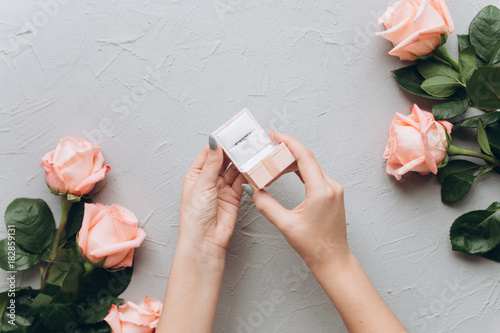 Valokuvatapetti Female hands open a letter with propose and hold a wedding ring on a gray background