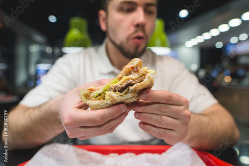 An appetizing sandwich in the hands of a man. A man eats a sandwich in a fast-food restaurant. Focus on the sandwich.