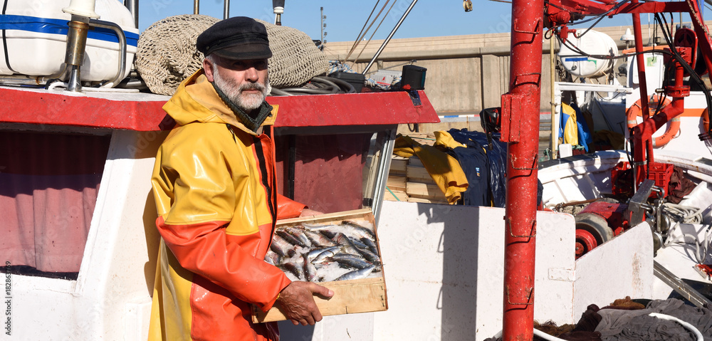 fisherman with a fish box inside a fishing boat - obrazy, fototapety, plakaty 
