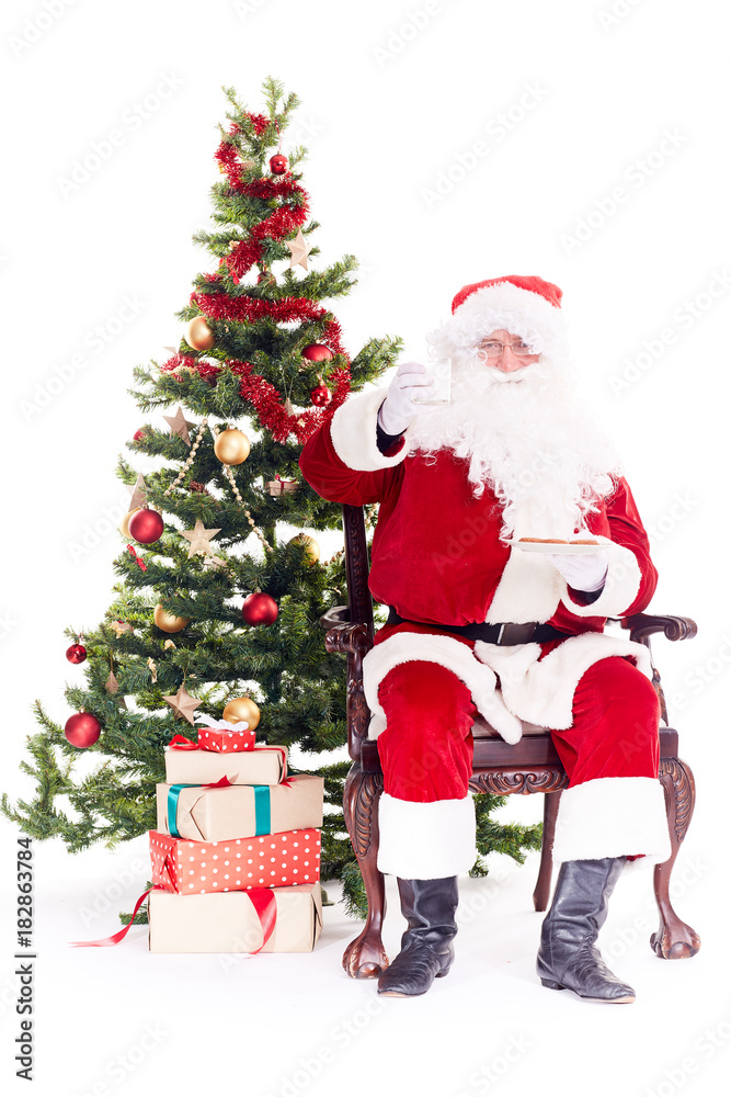 Portrait of Santa Claus sitting in chair next to Christmas tree, heap of gift boxes near him Portrait of Santa Claus sitting in chair next to Christmas tree, heap of gift boxes near him